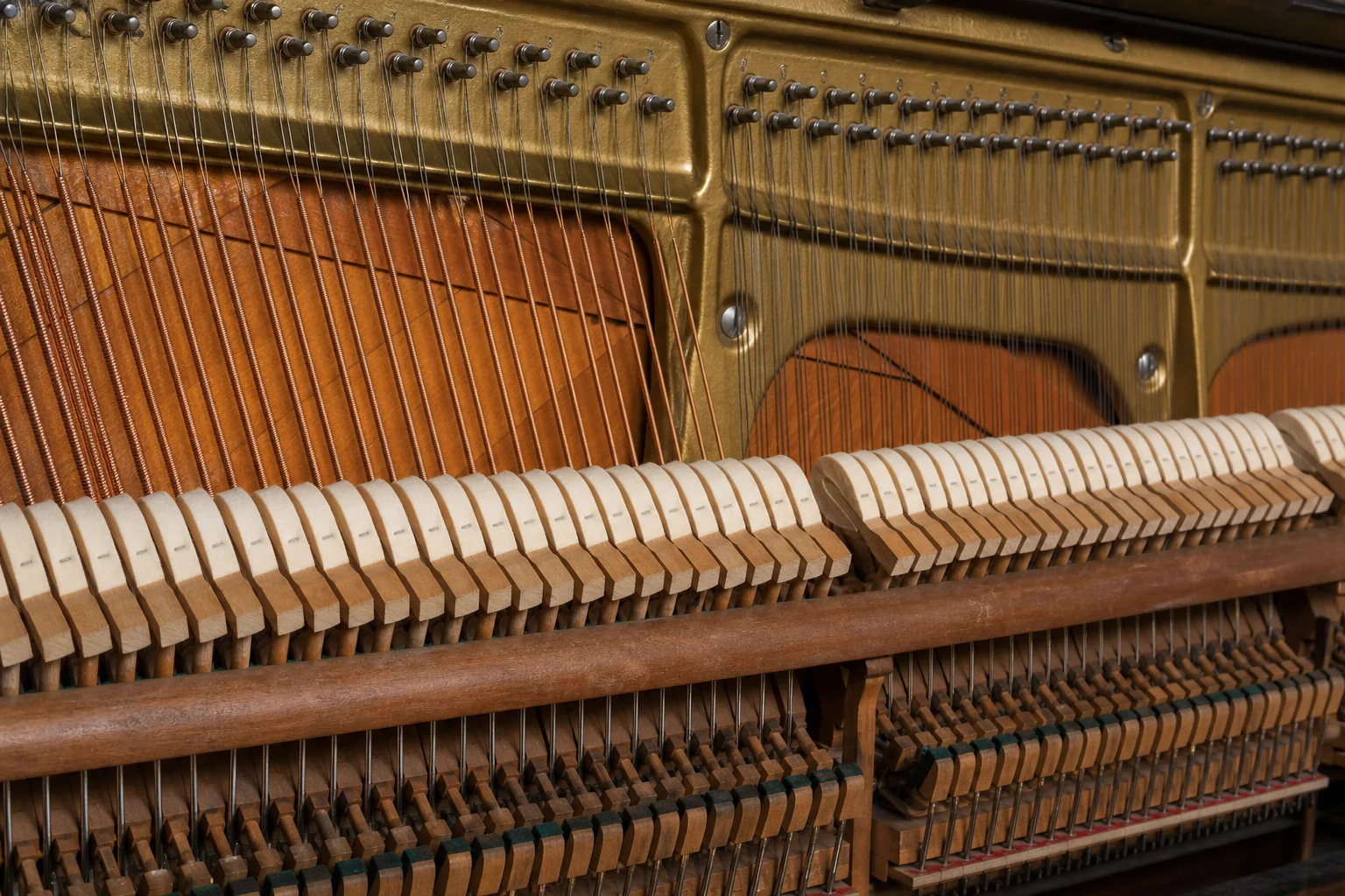 An open upright piano action showing rows of felt hammers, dampers, strings, the metal frame, and soundboard